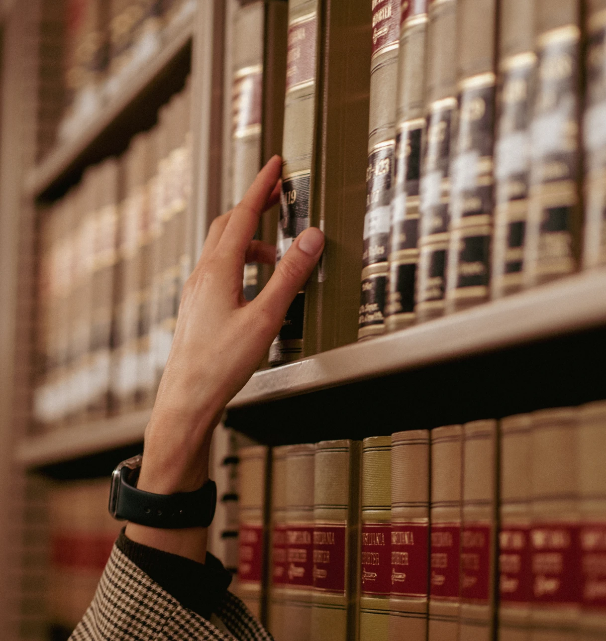 Hand reaching for book on shelf.